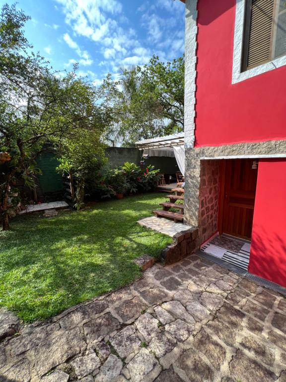 uma casa vermelha com um jardim verde em Suites Helena em Ilhabela