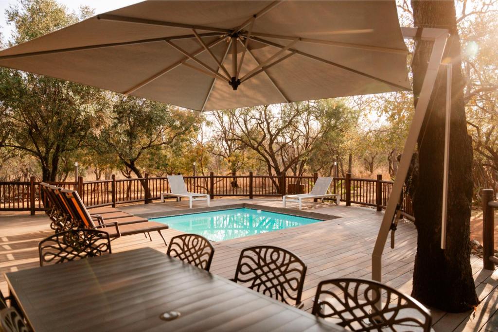 patio con tavolo, ombrellone e piscina di Zebula Lodge 118 a Mabula