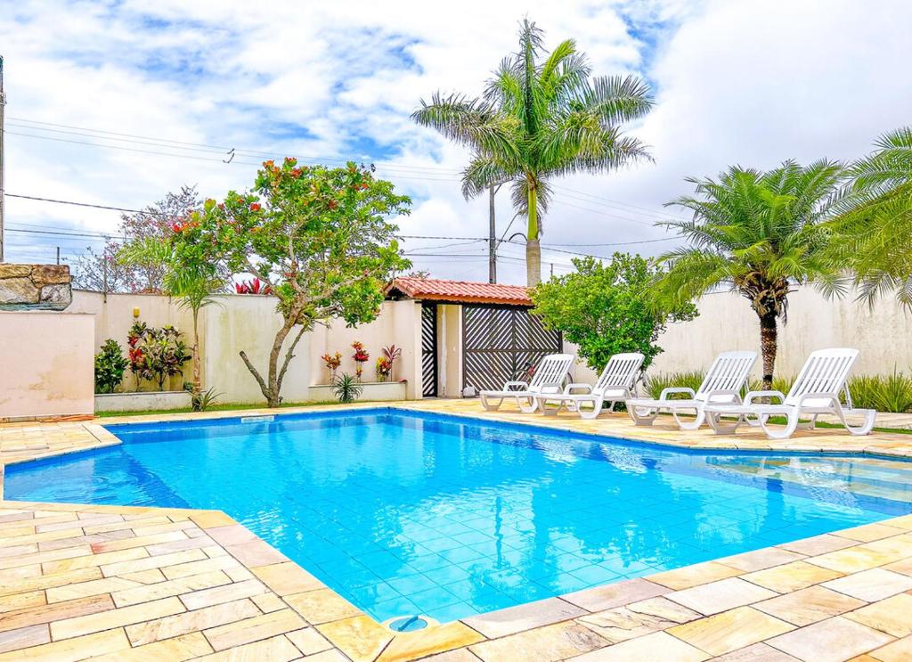 una piscina con sillas blancas y árboles en Casa com churrasqueira e piscina em Itanhaem, en Itanhaém