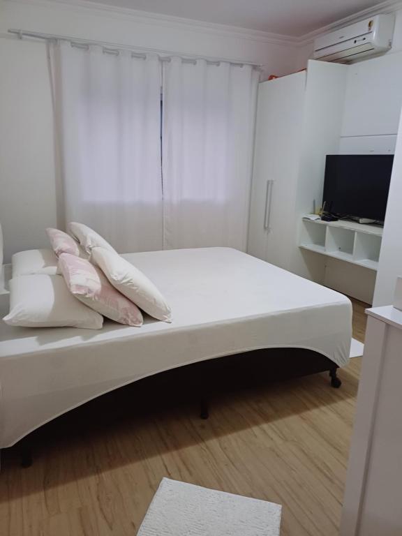 - une chambre blanche dotée d'un lit avec des oreillers et d'une télévision dans l'établissement Casa família, à Penha