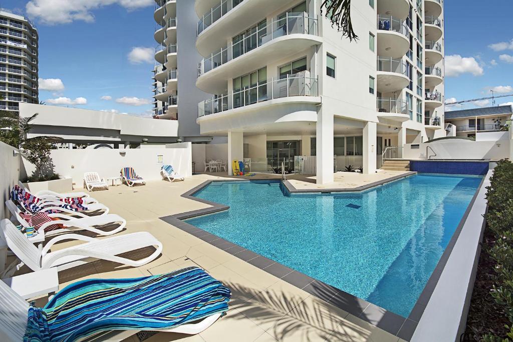 a swimming pool with lounge chairs in front of a building at Aqua Vista Resort in Maroochydore