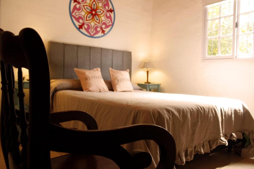 1 dormitorio con 1 cama con silla y reloj en Casa El Colibrí en Capilla del Monte