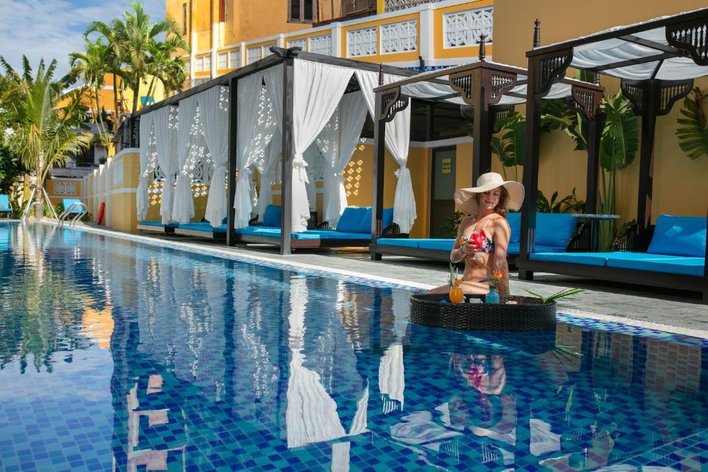 una mujer con sombrero sentada en una cesta junto a una piscina en La Charm Hoi An Hotel & Spa en Hoi An