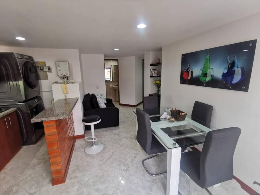 a living room with a glass table and a kitchen at Acogedor Apto Parque Sabaneta in Sabaneta