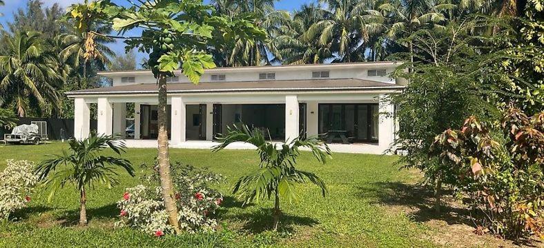 a white house with palm trees in a yard at Temata Estate Rarotonga in Rarotonga