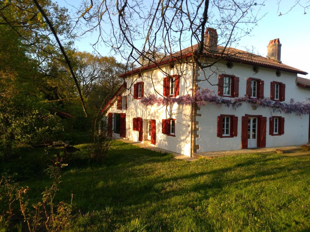 uma casa branca com janelas vermelhas num campo verde em Chambres Maison Labourdasse em Saint-Martin-de-Hinx