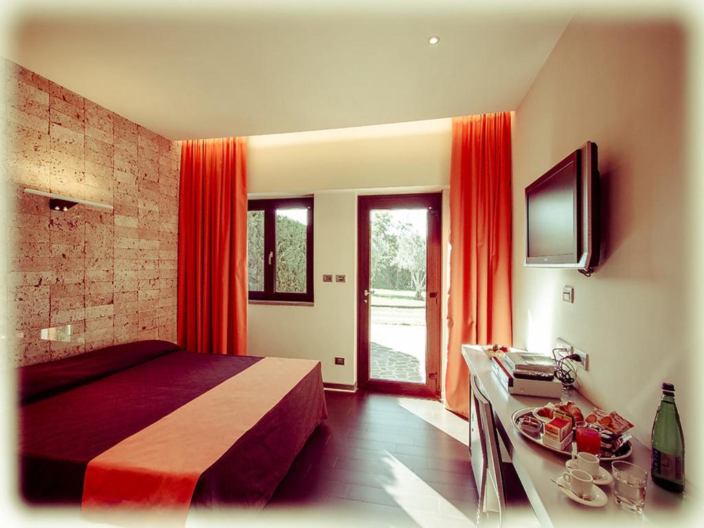 a bedroom with a bed with red curtains and a television at All Ways Garden Hotel & Leisure in Castel di Leva