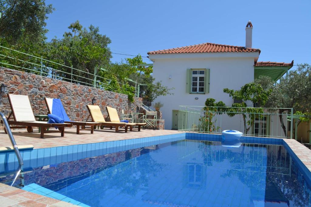 a pool with chairs and a house in the background at Villa Liogerma in Panormos Skopelos