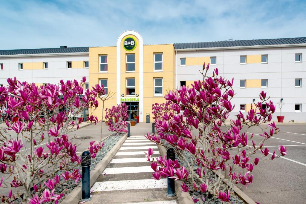 um edifício com flores cor-de-rosa em frente a um parque de estacionamento em B&B HOTEL Cholet Nord em Cholet