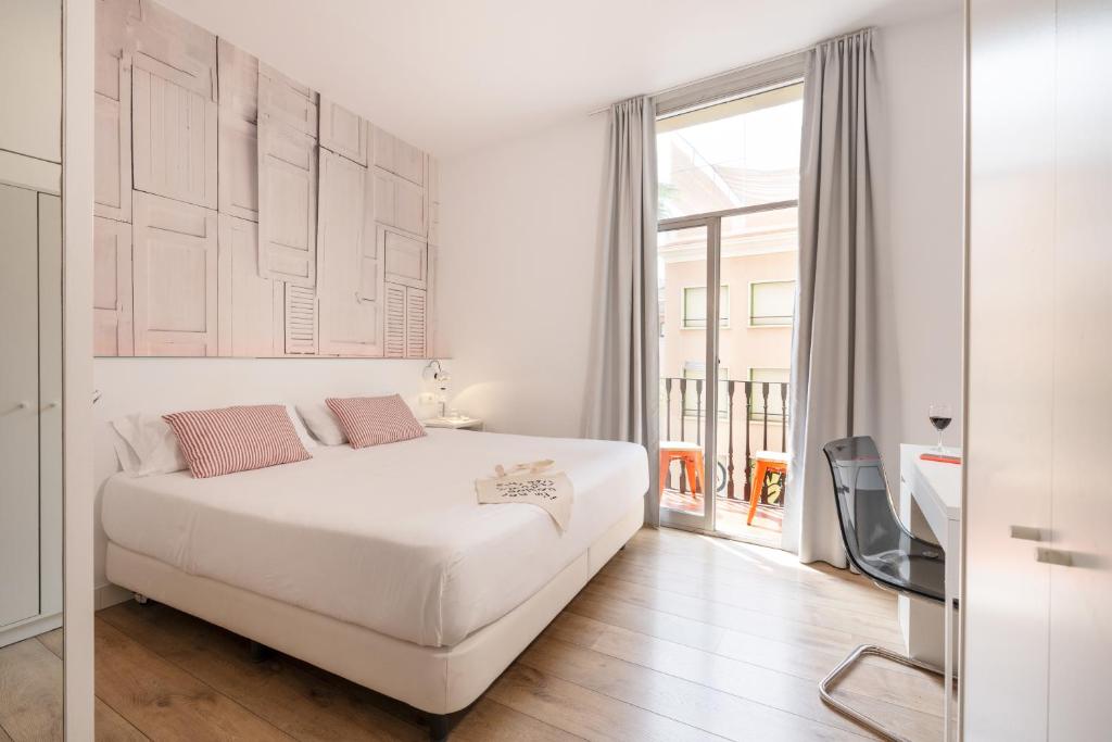 a white bedroom with a bed and a large window at Chic & Basic Tallers Hostal in Barcelona