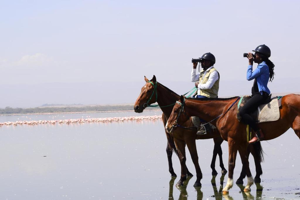 twee mensen paardrijden op het strand bij Lake Elmenteita Serena Camp in Elmenteita