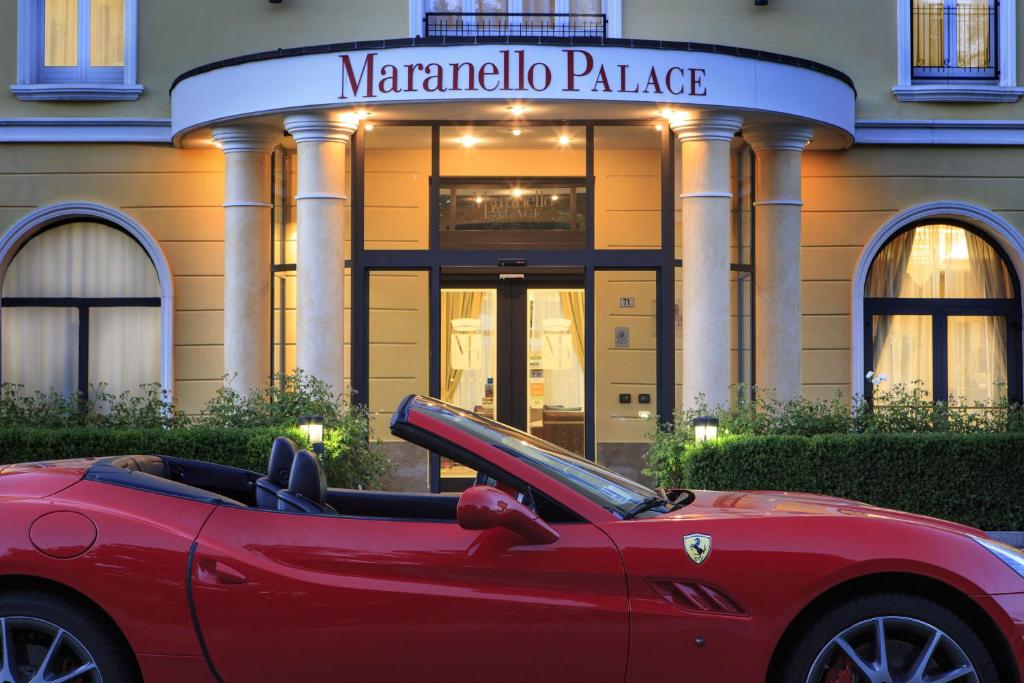 une voiture rouge garée devant un bâtiment dans l'établissement Maranello Palace, à Maranello