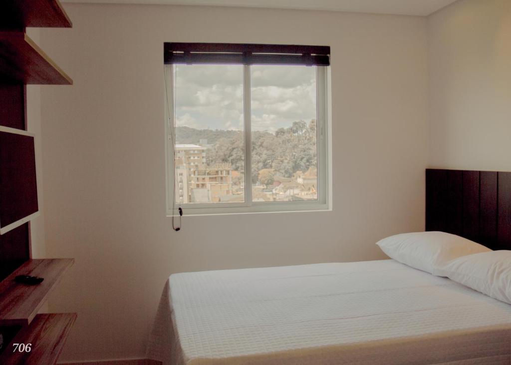 ein Schlafzimmer mit einem weißen Bett und einem Fenster in der Unterkunft Loft próximo a Vila Germânica 604 in Blumenau