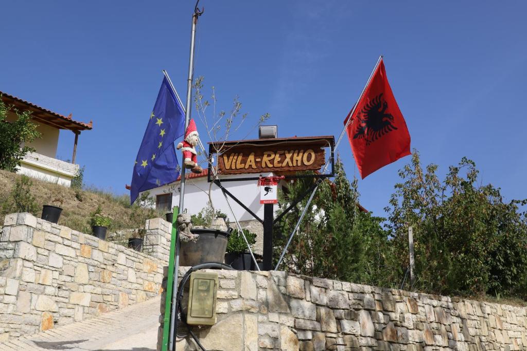 een straatbord en twee vlaggen op een stenen muur bij Villa Rexho in Berat
