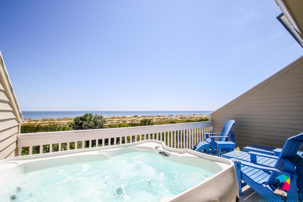 泰碧島的住宿－Beachfront Oasis At Tybee Island，一个带椅子和海滩的阳台的热水浴池