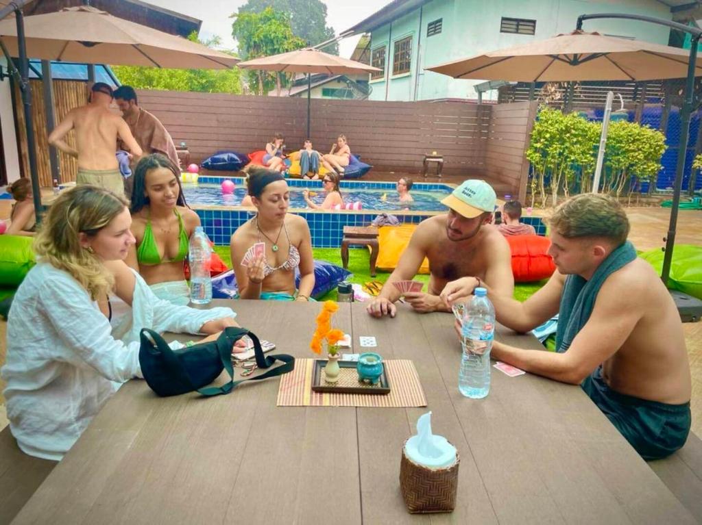 a group of people sitting around a table at a pool at K-Bunk Hostel Pai Walking Street in Pai