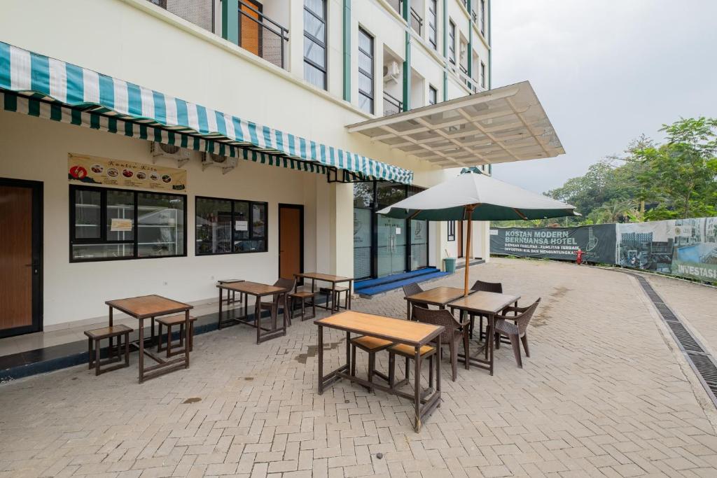 eine Terrasse mit Tischen und Stühlen und einem Sonnenschirm in der Unterkunft RedLiving Syariah Apartemen MKostel - Tower A1 Kencana Loka in Rancalutung