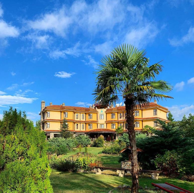 a palm tree in front of a large yellow building at Iliada Hotel Kaz Daglari in Kalkım