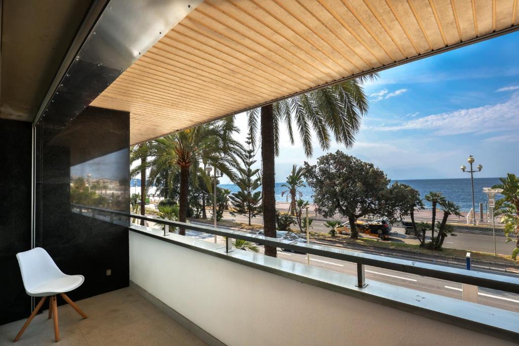 Cette chambre dispose d'une grande fenêtre avec une chaise blanche et une vue sur l'océan. dans l'établissement Incroyable vue mer, 2 pièces refait à neuf avec piscine sur le toit/ WIFI/AC, à Nice