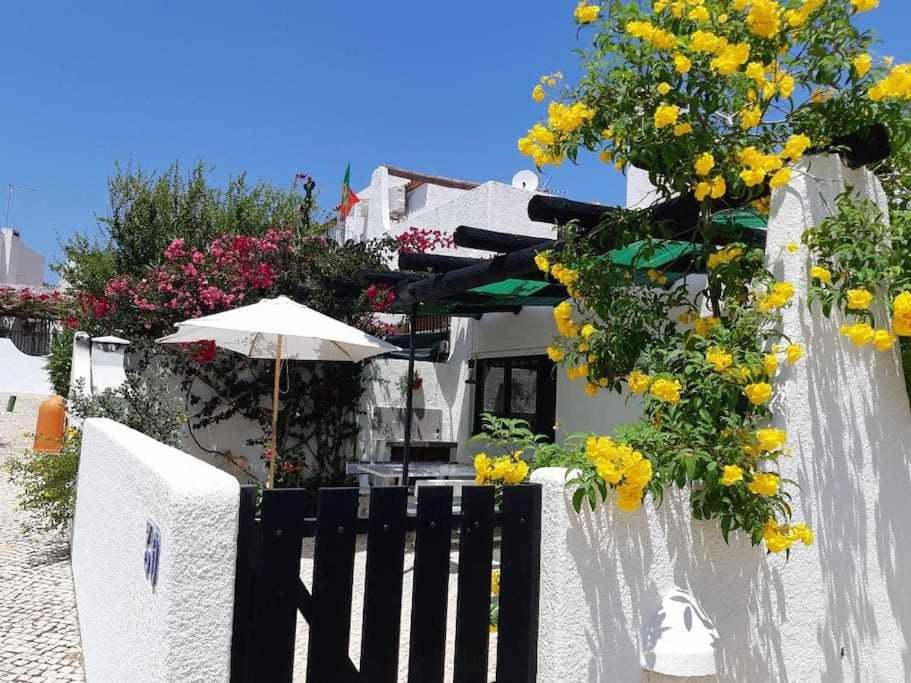 a white fence with yellow flowers and an umbrella at Green House by FHR estacionamento e WI-FI in Quarteira
