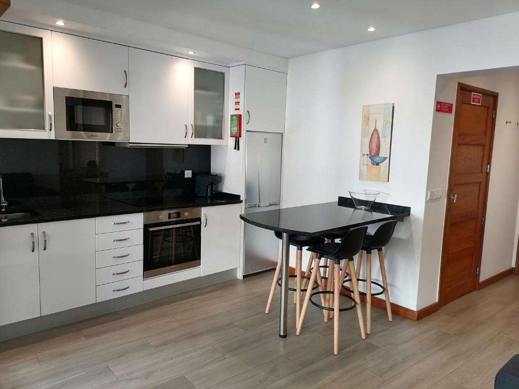 uma cozinha com armários brancos, uma mesa preta e bancos em Beach House na Póvoa do Varzim