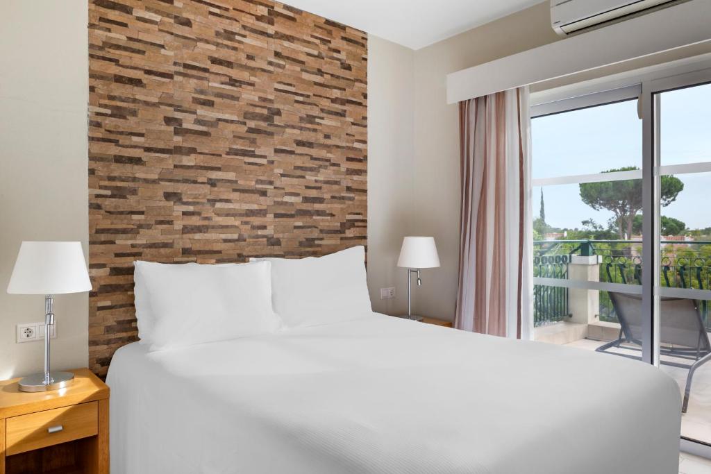 a bedroom with a white bed and a brick wall at Vilar do Golf in Quinta do Lago