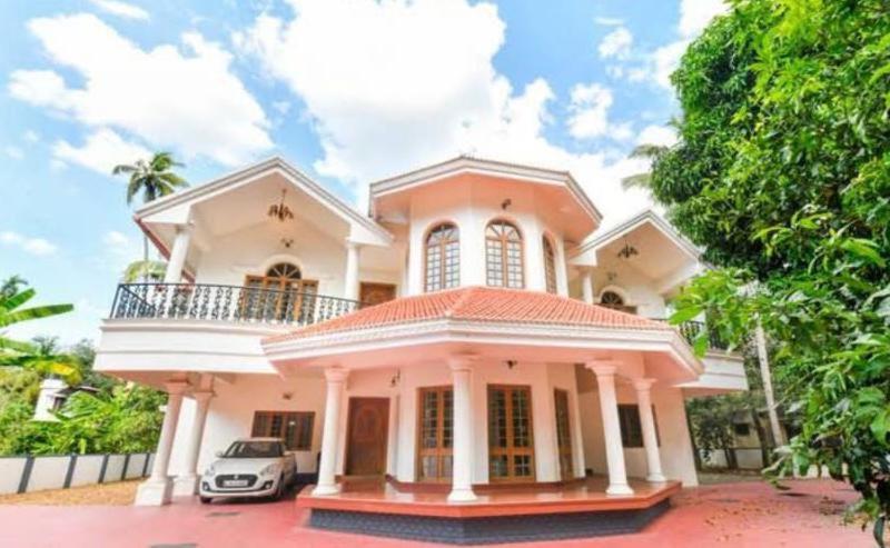 une maison rose avec une voiture garée devant elle dans l'établissement Palatial villa in Kottayam town with 6 bedrooms, à Kottayam