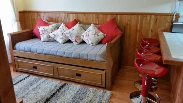 a bed with pillows on it with a table and a stool at Departamento Acogedor Parque Suizo 800 Pucon in Pucón