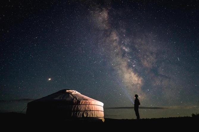 Kyzylkum Nights Camp & Family Yurt في Nurota: رجل يقف أمام خيمة تحت سماء الليل
