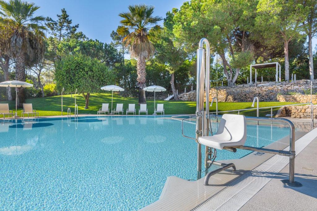 a swimming pool with a white chair and trees at Vilar do Golf in Quinta do Lago