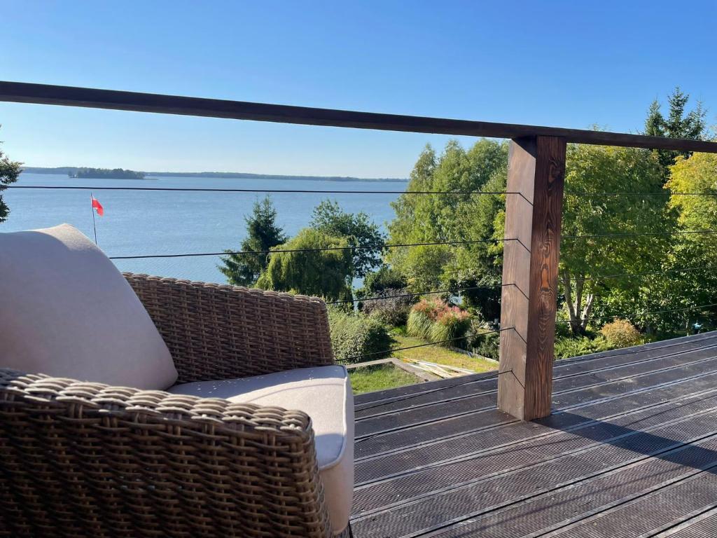 a wicker chair on a deck with a view of the water at Apartamenty Fuleda nad jeziorem Dobskim Mazury Holiday in Fuleda