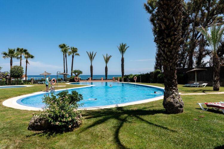 une grande piscine avec des palmiers et l'océan dans l'établissement Don Juan - Apartament - Manilva, à Manilva