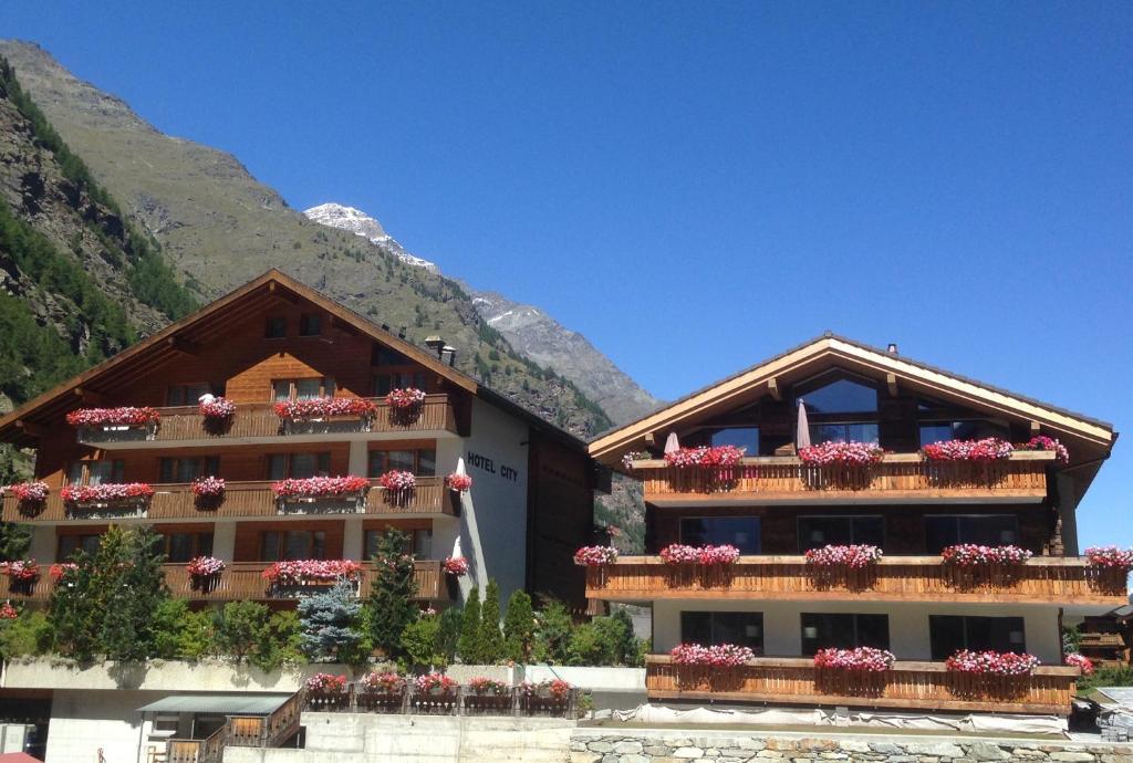 a building with flowers on the balconies of it at Hotel City in Täsch