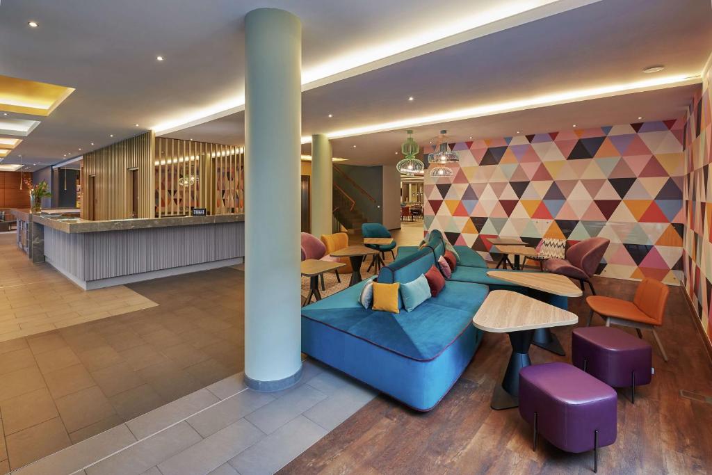 eine Lobby mit einem blauen Sofa sowie Tischen und Stühlen in der Unterkunft Hampton by Hilton Berlin City West in Berlin