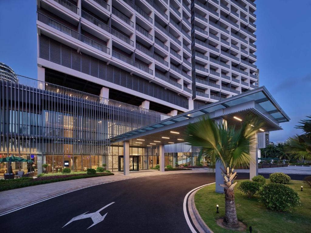 a large building with a palm tree in front of it at Hilton Garden Inn Sanya in Sanya