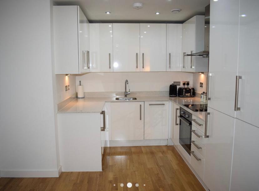 cocina blanca con suelo de madera y armarios blancos en Wembley Stadium Luxurious Apartment, en Londres