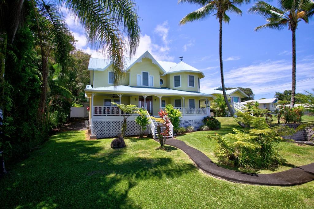 a yellow house with palm trees in the yard at Grand Melemele home in Pepeekeo