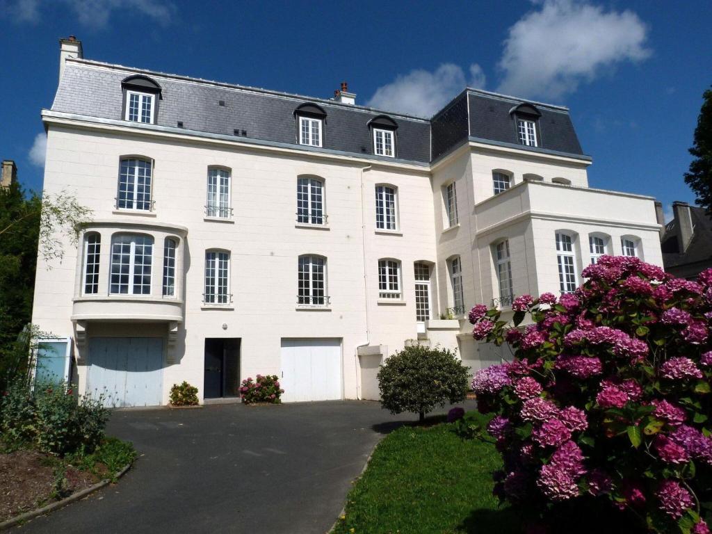 une grande maison blanche avec des fleurs devant elle dans l'établissement Comfortable holiday apartment on the 2nd floor of an elegant manor house, à Coutances