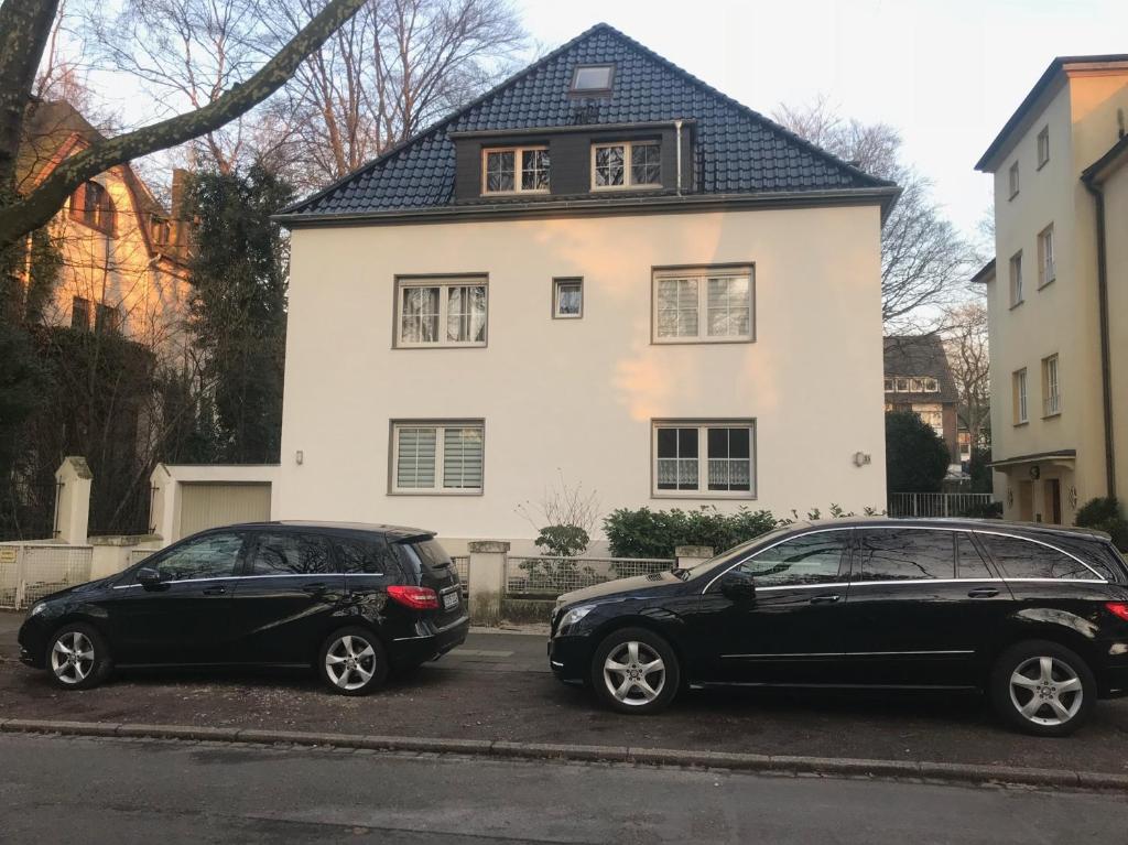 zwei Autos, die vor einem weißen Haus geparkt sind in der Unterkunft Erdgeschoss Apartment am Park im Theaterviertel in Oberhausen in Oberhausen