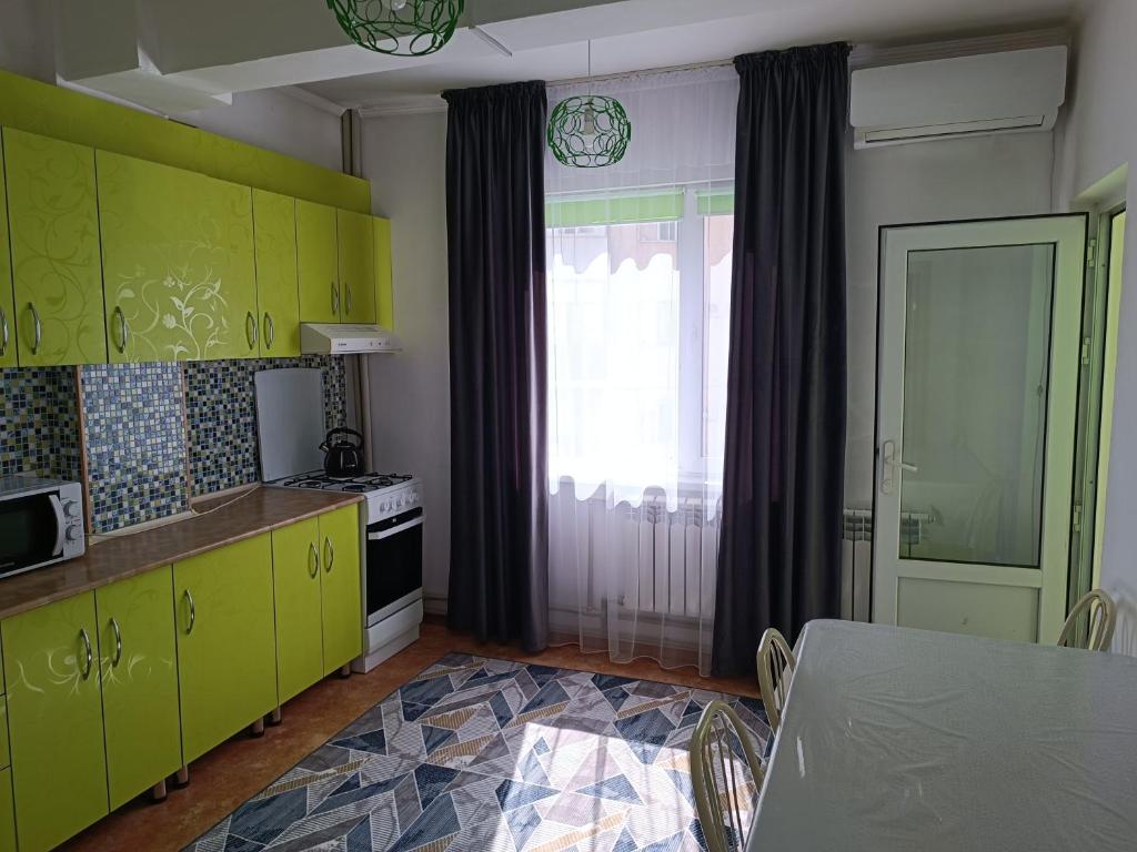 kuchnia z żółtymi szafkami, stołem i oknem w obiekcie Уютная квартира w mieście Taraz