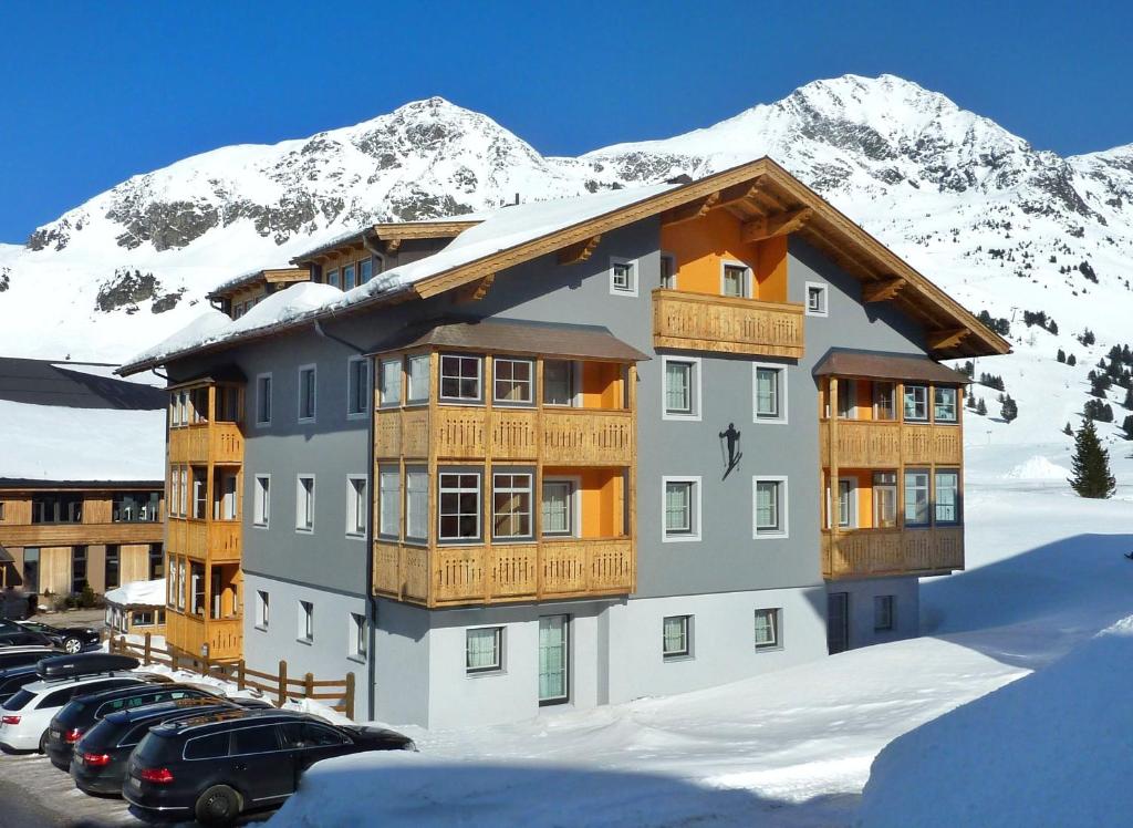 ein Gebäude mit Autos auf einem Parkplatz mit schneebedecktem Berg in der Unterkunft Aparthotel Bernhof in Obertauern