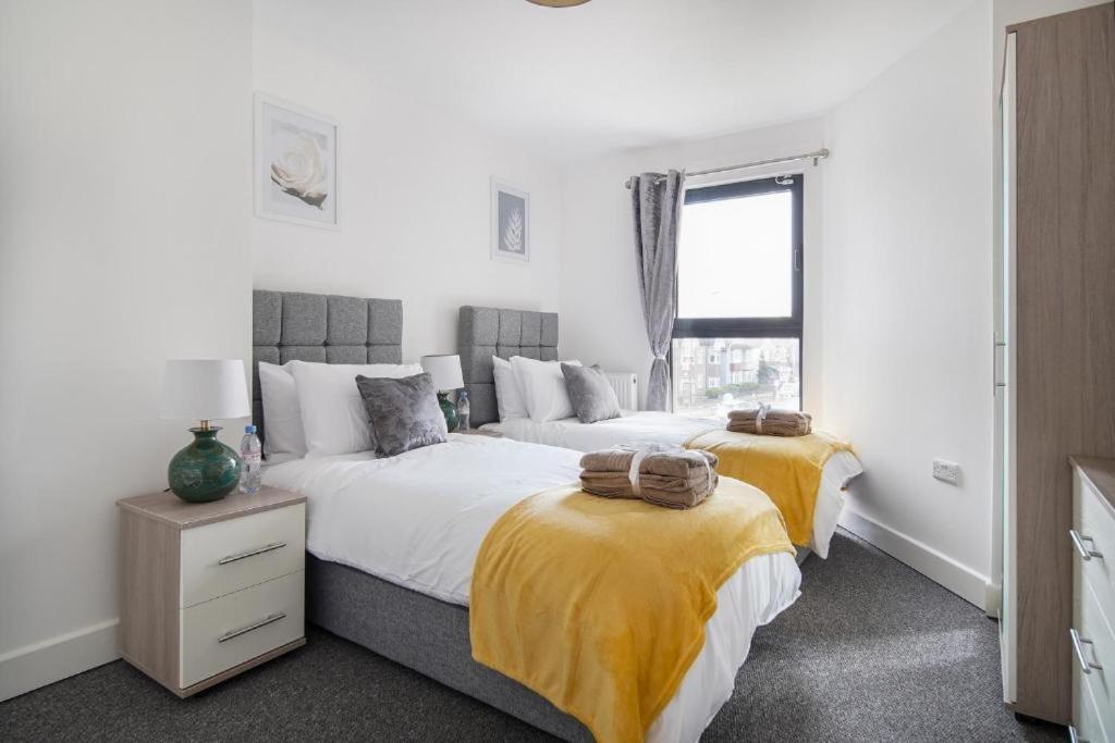 um quarto com duas camas com cobertores amarelos e uma janela em Heathrow Haven: Stylish Apartments in the Heart of Slough em Slough