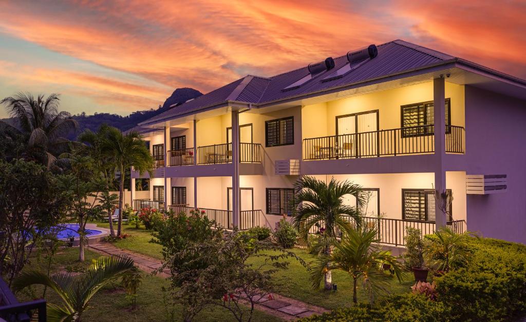 Creole Breeze Self Catering Apartments في ماهي: مبنى مع غروب الشمس في الخلفية