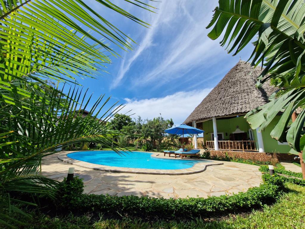 a swimming pool in front of a house with an umbrella at Paradiesische Villa Maisha Mazuri mit Pool. Terrasse und Personal in Diani Beach