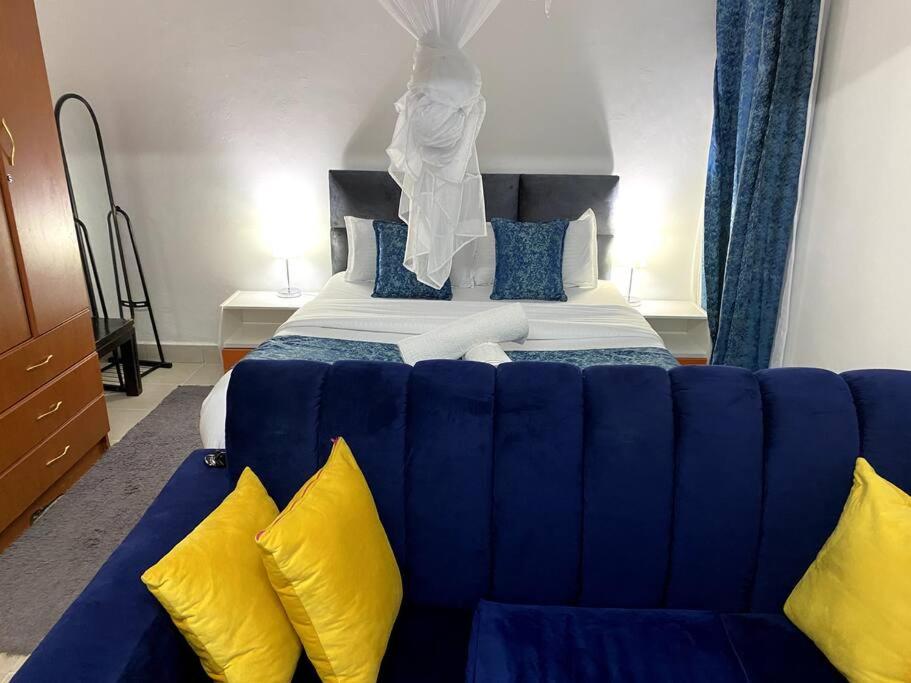 a blue couch in front of a bed with yellow pillows at Cottage with AC in Kisumu