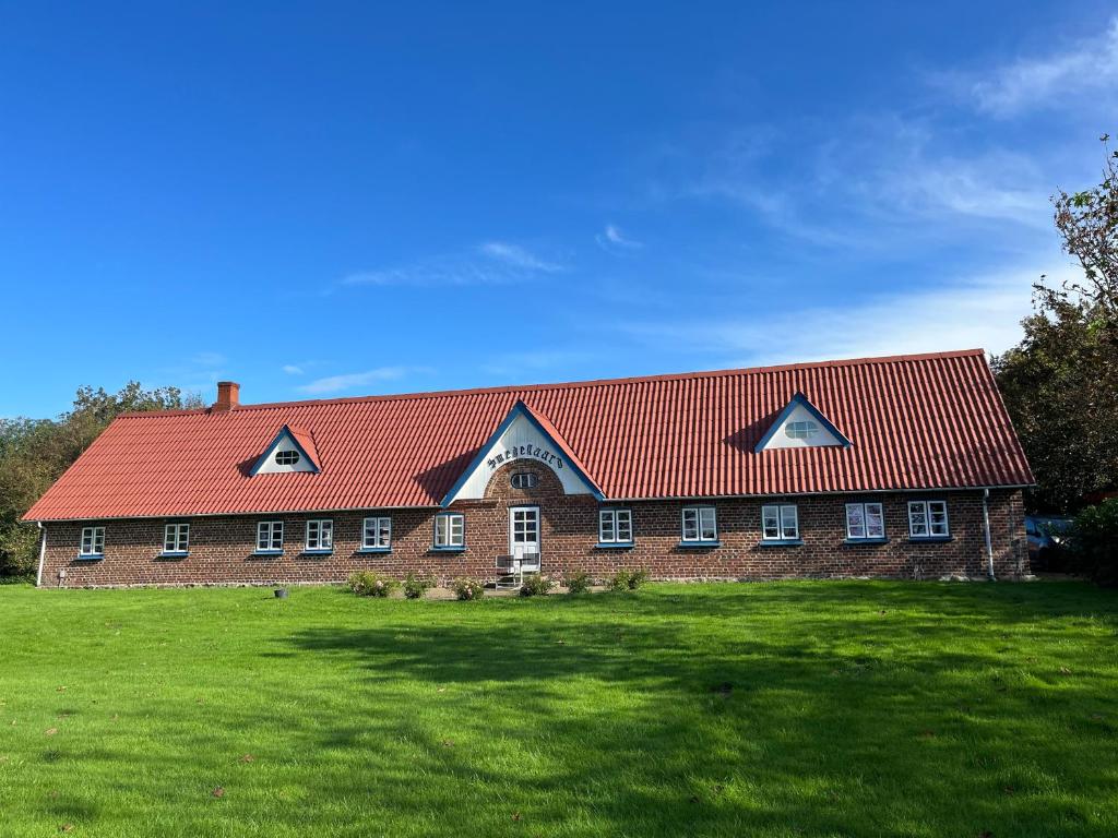 un grand bâtiment en briques avec un toit rouge dans l'établissement Smedegaard værelser, à Skjern