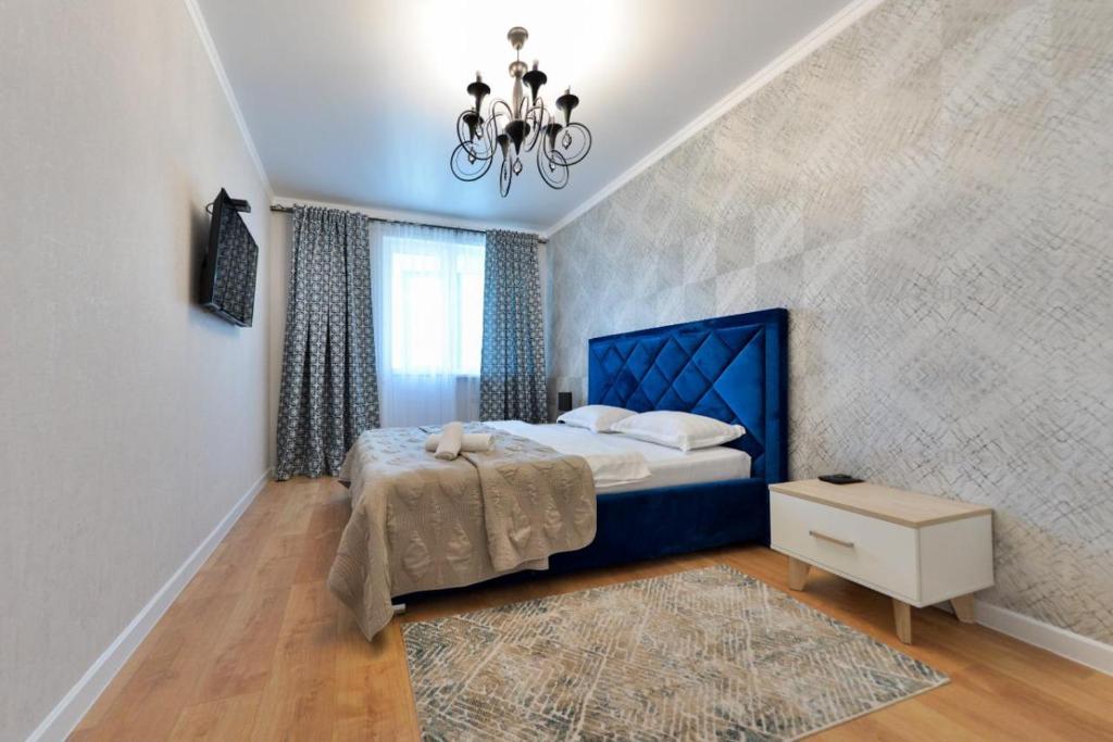 a bedroom with a blue bed and a chandelier at Apartment Lazurniy 7Б in Astana