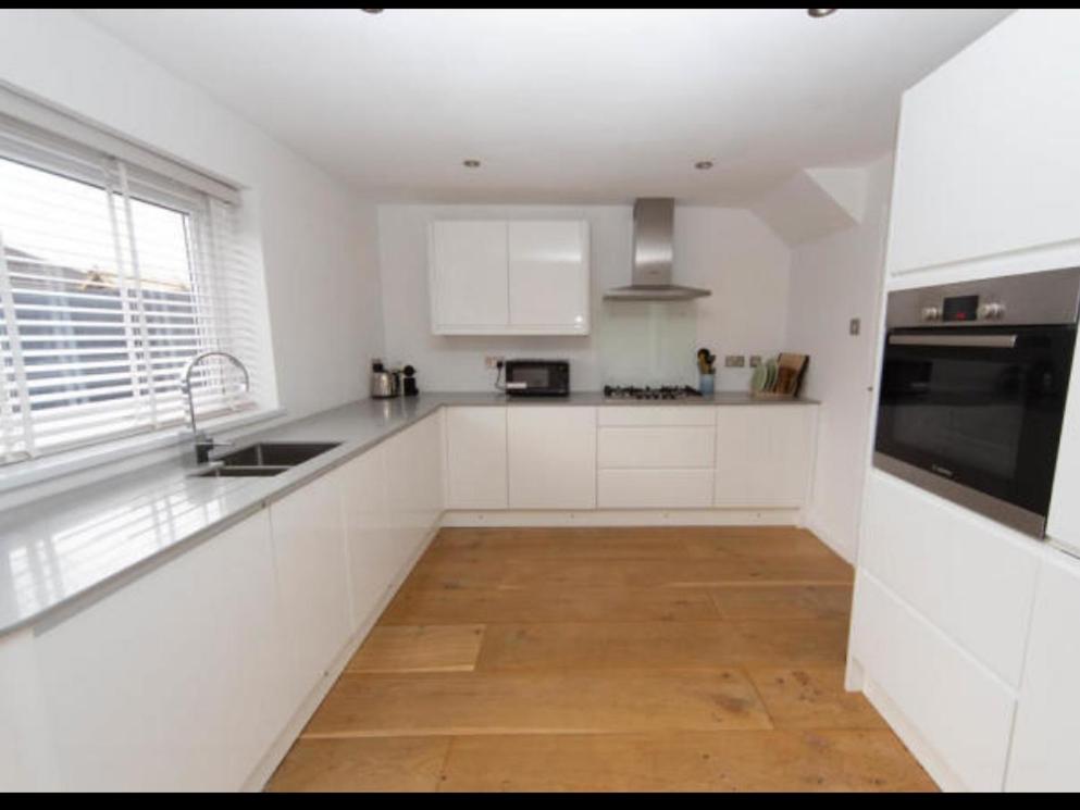 a kitchen with white cabinets and a wooden floor at Sunny room in a modern house in Cardiff