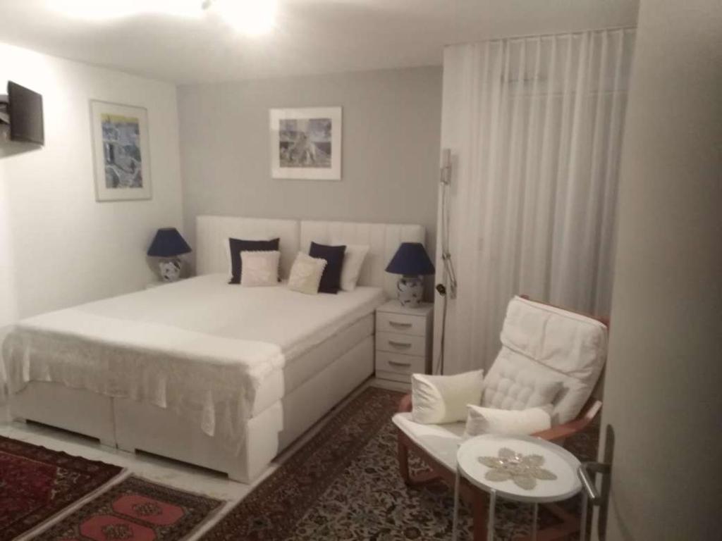 a white bedroom with a bed and a chair at STUDIO "Helvetia Star" in Zürich-Pfaffhausen in Pffaffhausen