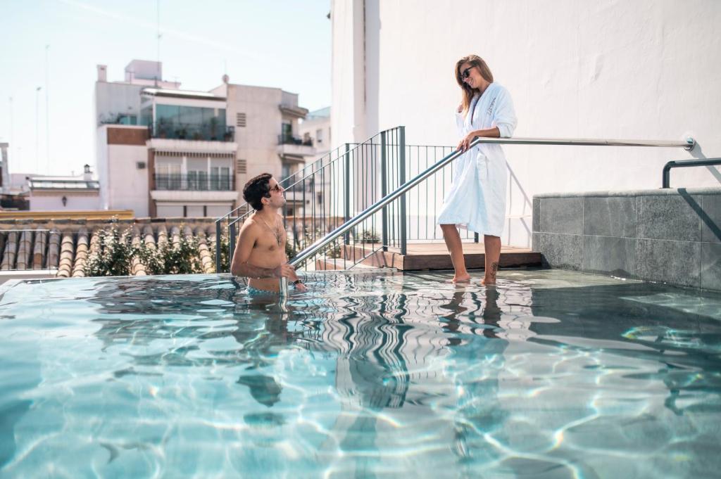 un homme et une femme debout dans une piscine dans l'établissement Legado Magdalena Hotel, à Séville